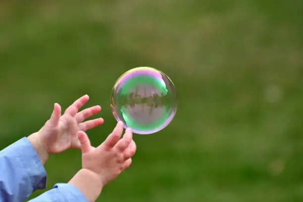 Photo of Large Bubble Being Caught by a Young Child Outside in the Spring Close Up Abstract