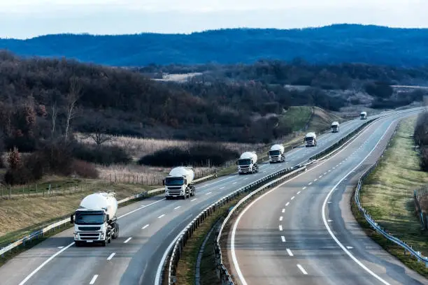 Fleet of White Tank truck or cistern as a convoy on a Highway through the rural landscape. 

Business Transportation And Trucking Industry.