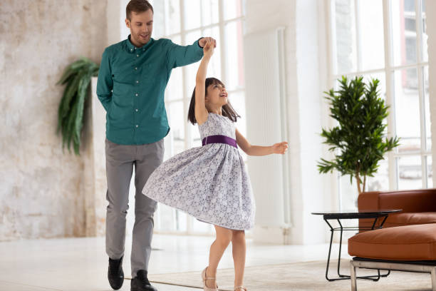 Loving dad dancing swaying smiling preschooler daughter Happy young dad dance swirl cute little daughter in beautiful princess dress at home, loving father have fun with excited preschooler girl child, engaged in funny activity, swaying in living room dancing dad stock pictures, royalty-free photos & images