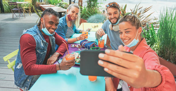 freunde machen selfie in einem bar-restaurant mit gesichtsmaske auf in coronavirus-zeit - jugendliche, die spaß mit getränken und snacks draußen mit neuen regeln nach viruspause haben - face time stock-fotos und bilder