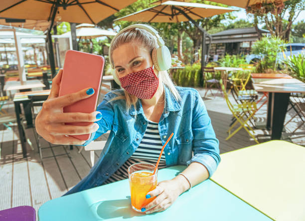 mädchen in bar nehmen ein selfie mit einem smartphone mit ihrer gesichtsmaske als schutz für coronavirus zeit - teenager chillen draußen und genießen ein kaltes getränk - lebensstil von covid-19 - face time stock-fotos und bilder