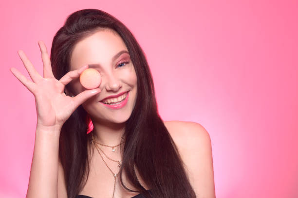 istock Girl eats macaroon, model on a pink background eats a sweet, sugar diet. Brunette with pink make-up, addicted to food. 1236321454