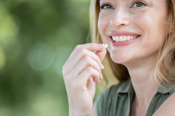 Smiling woman holds vitamin up to mouth Smiling woman holds vitamin up to mouth vitamin a nutrient stock pictures, royalty-free photos & images