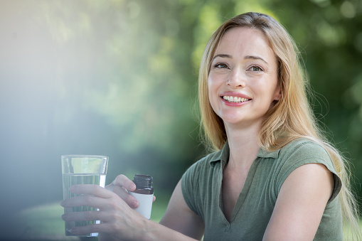 Woman smiles while holding glass of water and vitamin bottle