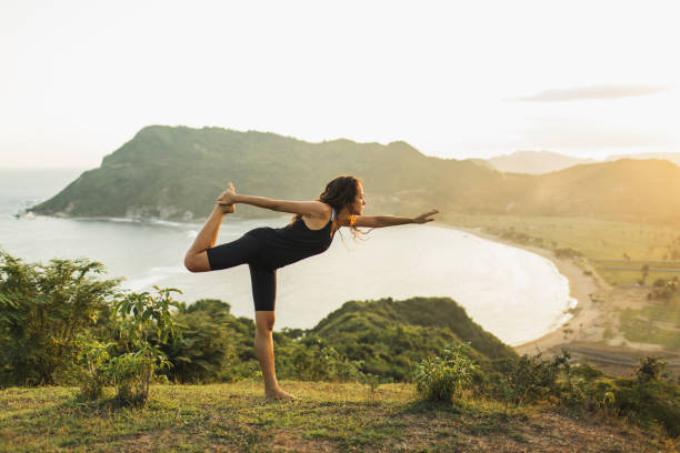 istock Young woman practicing yoga poses at sunset with beautiful ocean and mountain view. Sensitivity to nature. Active lifestyle. Spiritual and emotional concept. 1236471698