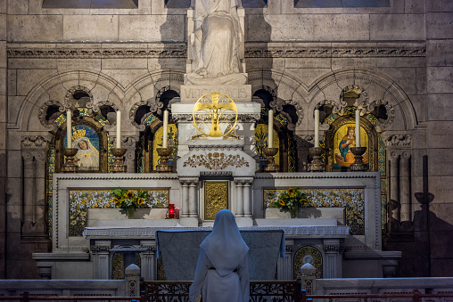 A nun praying in front of the statue of Saint Mary of the Basilica of Sacre Coeur (designed by Paul Abadie, 1914) - a Roman Catholic Church and minor basilica, dedicated to Sacred Heart of Jesus.