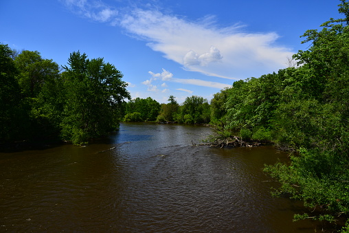 The Fox River in Rochester Wisconsin with blue clouded skies above.  The high contrast vista evokes a peaceful feeling.