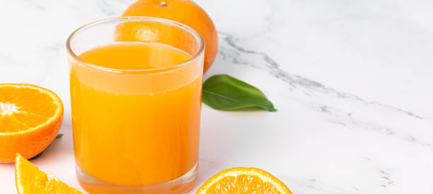 istock Fresh orange juice in glass and oranges fruit on white marble table banner background with copy space 1236632337