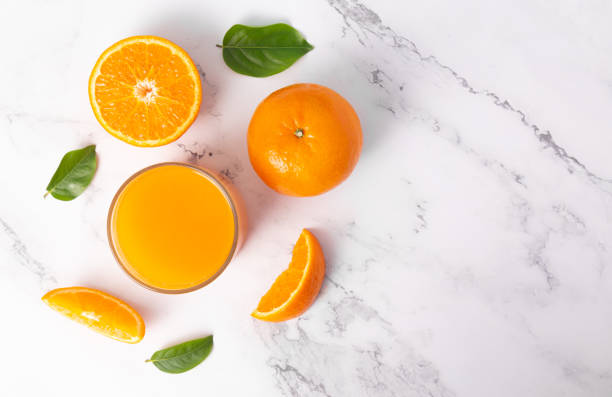 istock Fresh orange juice in glass and oranges fruit on white marble table background top view with copy space 1236664036