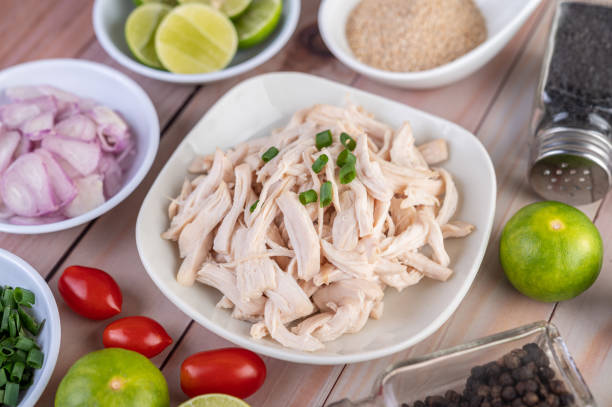 istock Boiled chicken cut into pieces in a white dish, along with lemons, chilies, lemongrass, red onions, chopped onions, tomatoes, sesame, roasted rice, and pepper on a wooden table. 1236742982