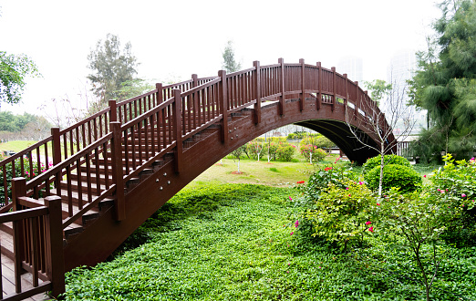 Wooden arched bridge over green bush.