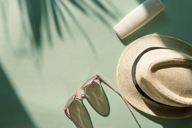 istock Sun hat, glasses and spf cream or lotion unbranded package on light blue background with palm tree leaf shadow, top view 1236853839