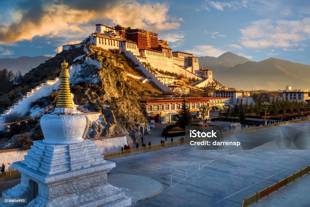 Potala golden hour sunrise with clouds Dramatic morning sunrise scene of the Potala Palace in Lhasa Tibet with pilgrims walking around the temple along the road in front of the monastery.  The traditional home of the Dali Lama. Lhasa - East Asia Stock Photo