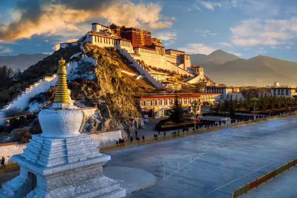 Dramatic morning sunrise scene of the Potala Palace in Lhasa Tibet with pilgrims walking around the temple along the road in front of the monastery.  The traditional home of the Dali Lama.