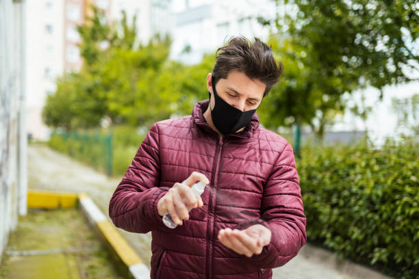 istock Millenial Man in Face Mask Cleaning his Hand with Antiseptic 1236860185