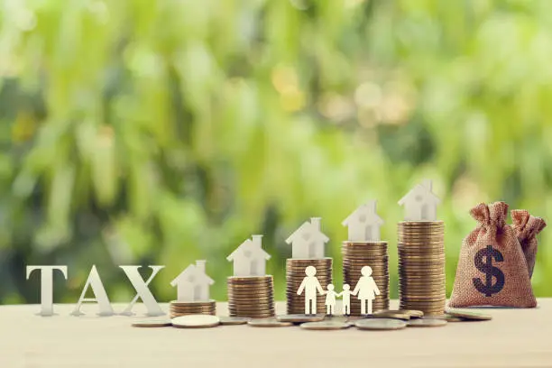 Photo of Family members, house, dollar money bags on rows of rising coins. Concept family tax benefit, residential property or estate taxt depicts home equity loan, reverse mortgage