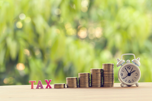 Colorful word tax, Alarm clock ,rows of rising coins on a table. Concept tax collection, investment and capital gain tax depicts financial charge levy imposed upon a taxpayer or individual