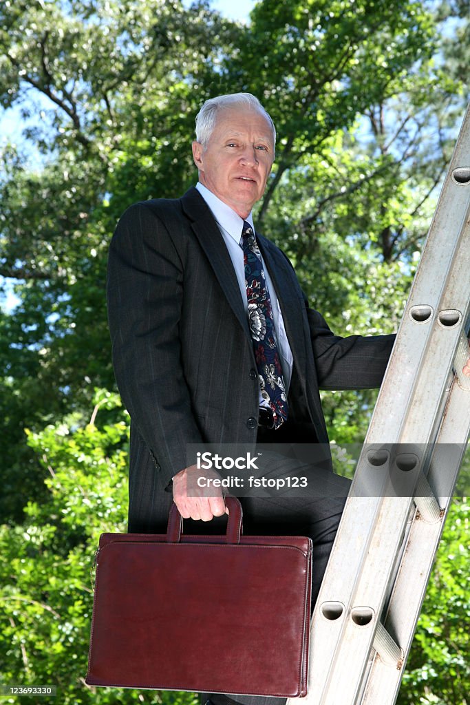 Mature man in business suit climbing ladder Mature man in business suit with briefcase climbing a metal ladder.  He is looking at the camera. Achievement Stock Photo