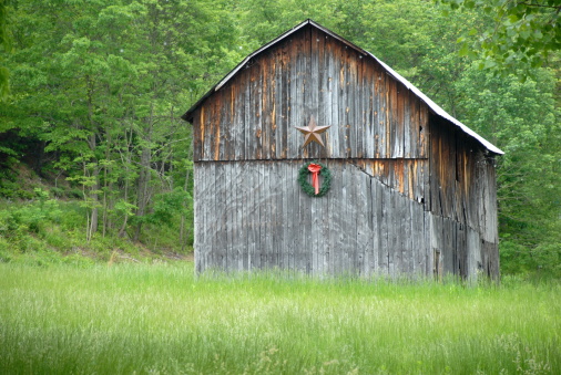 A weathered, wooden barn decorated with a simple Christmas wreath awaits the winter season.  \t\t