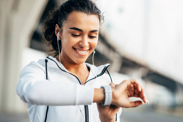 mujer sonriente comprobando su actividad física en smartwatch. joven atleta que busca en el seguimiento de la actividad durante el entrenamiento. - city street audio fotografías e imágenes de stock