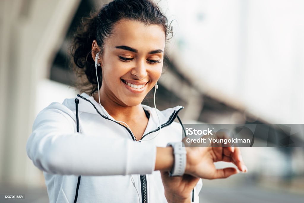 Smiling woman checking her physical activity on smartwatch. Young female athlete looking on activity tracker during training. Exercising Stock Photo