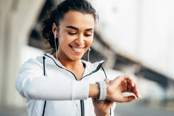 Photo of Smiling woman checking her physical activity on smartwatch. Young female athlete looking on activity tracker during training.