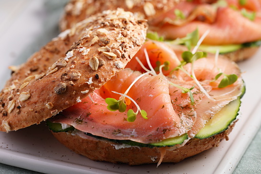 Two bagel sandwiches with sliced salt salmon, cream cheese, cucumber, and micro greens closeup