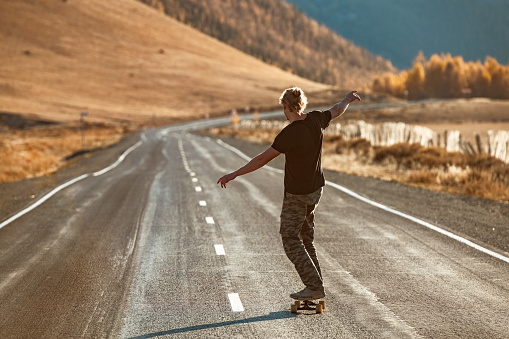 Lonely unrecognized skateboarder rides on longboard at straight mountain road