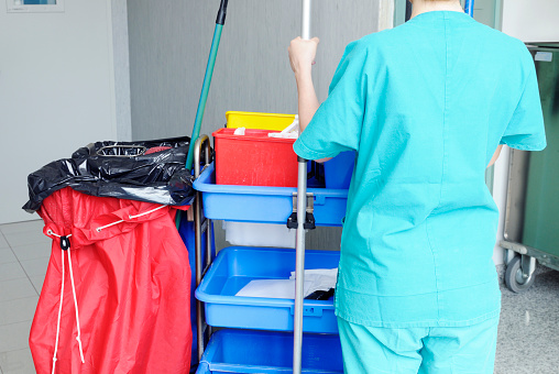 cleaner woman with mop and uniform cleaning corridor floor of hospital.