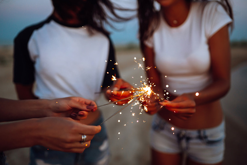 The sparklers in the hands of young girls on the beach. Three girls enjoying party on beach with sparklers. Summer holidays, vacation, relax and lifestyle concept.