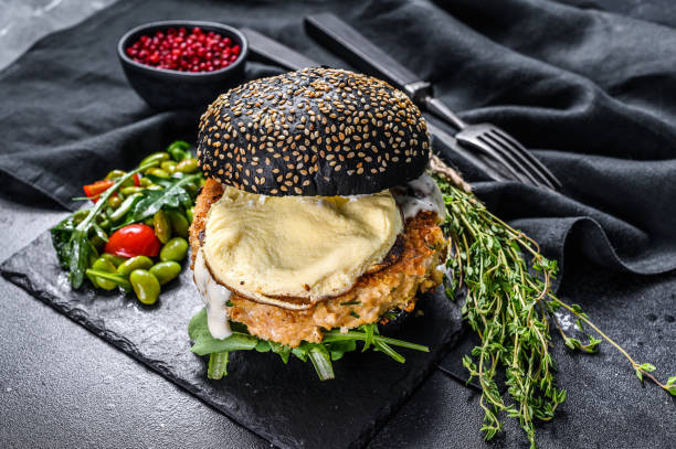istock FishBurger with black brioche bun, omelette, fish cutlet and arugula. Black background. Top view 1237139983