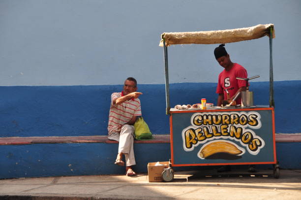So much of Cuban life takes place on the city streets: negotiating with ambulant vendors, gossiping and board games with neighbors, playing music for passersby, etc. Here an older man seated on a bench gestures to the vendor next to him. Photos taken in Santiago de Cuba in January 2017.