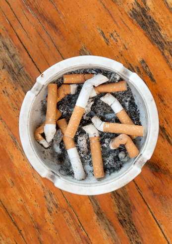 White ashtray full of cigarettes at wooden background