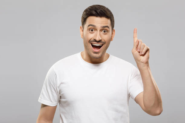 istock Young man in white t-shirt pointing up with his finger feeling excited with open mouth, showing benefit of commercial offer, isolated on gray background 1237257795