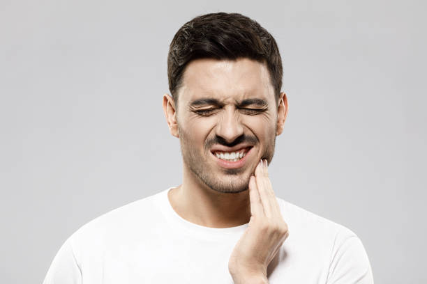 istock Young man suffering from strong toothache, holding eyes closed, touching his jaw to ease pain, feeling helpless and miserable, isolated on gray background 1237257816