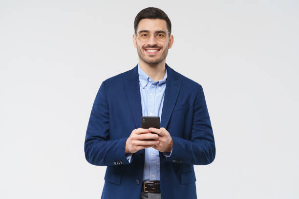 istock Young business man holding smartphone, exchanging messages with friends and colleagues, looking at camera with happy smile, isolated on gray background 1237257822