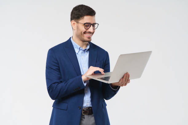 istock Young male teacher wearing eyeglasses, holding open laptop, looking at content on screen with happy smile, isolated on gray background 1237258332
