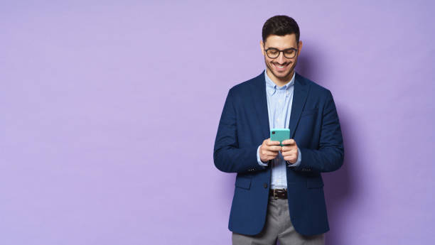 眼鏡とフォーマルな服を着た若いビジネスマンの水平バナー、電話でテキストメッセージ、画面で幸せな笑顔、紫色の背景に隔離 - business blue business person businessman ストックフォトと画像
