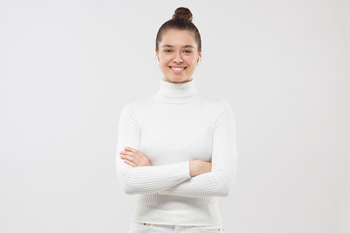 Young female dressed in white clothes, hair tied in bun, smiling happily, feeling confident in professional sphere, isolated on gray background