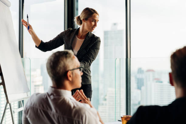 istock Businesswoman coach speaker wear suit give blank flipchart presentation, Speaker presenter consulting training persuading employees client group, Business meeting, seminar, presentation concept. 1237270717