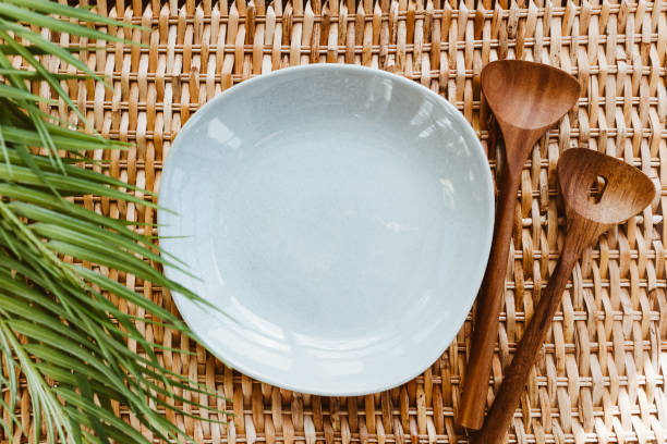 istock Top view of an empty ceramic plate with wooden kitchen utensils and palm leaf on a rattan background. Summer and eco friendly concept. 1237292418
