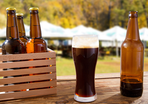 cup of dark beer and bottle on wooden table on blurred summer background