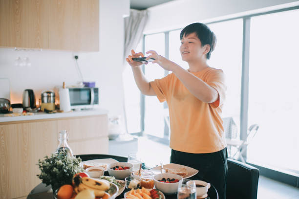 una mujer china asiática tomando fotos directamente arriba en su desayuno saludable con naranja fruta, fresa, verdura, plátano, huevos, pan tostado, manzana de yogur y mermeladas en la mesa de comedor - apple portion red freshness fotografías e imágenes de stock