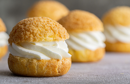 Chou pastry biscuits filled with whipped cream on grey background. Concept: bakery, french dessert. Selective focus.