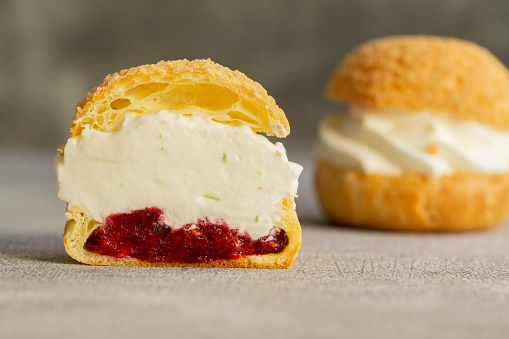 Choux pastry cookies filled with whipped cream and raspberry jelly on gray background. Concept: bakery, french dessert. Selective focus.