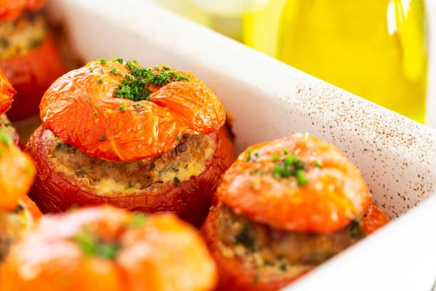 Close-up on French stuffed tomatoes with meat, bread crumbs, and herbs in a white dish, aside a bottle of olive oil. stock photo
