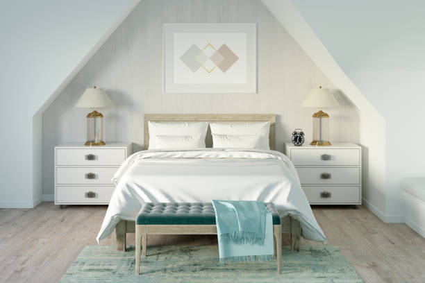 istock Modern mansard bedroom with a horizontal poster under the bed between bedside tables with lamps and a bench by the bed. Front view. 1237390601