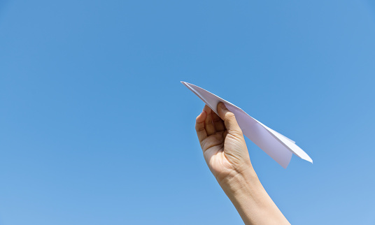 Woman hand holding paper airplane under blue sky.