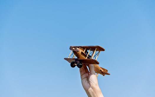 Woman hand holding model airplane under blue sky.