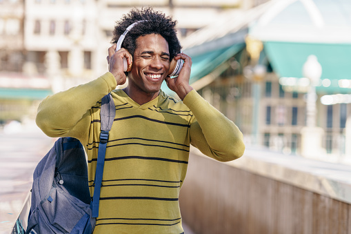 Cuban Black man with afro hair listening to music with wireless headphones sightseeing in Granada, Andalusia, Spain.